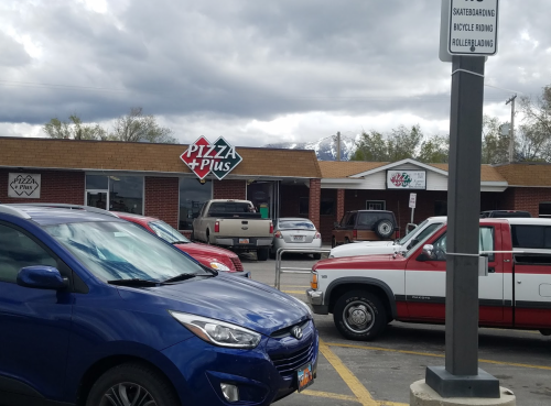 A parking lot with cars in front of a pizza restaurant, under a cloudy sky with mountains in the background.