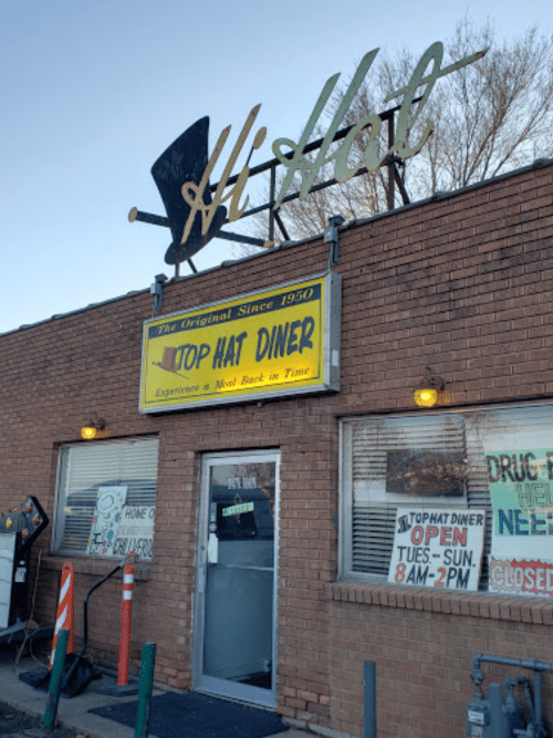 Sign for Top Hat Diner, established in 1950, with a retro design and open hours displayed on the front.