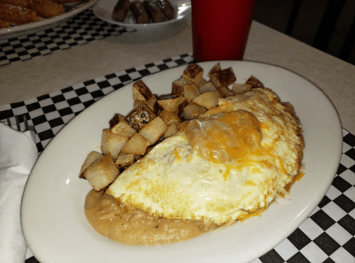A plate of an omelette topped with cheese, served with seasoned potatoes and a side of refried beans.