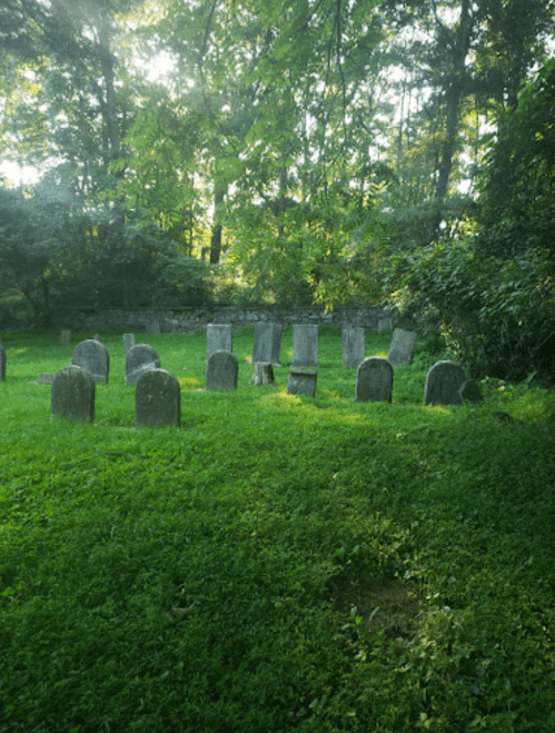 A serene graveyard with weathered tombstones surrounded by lush green grass and trees.