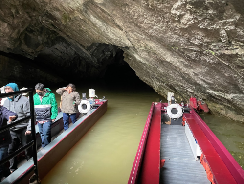 Two boats inside a dark cave, with people boarding and the water reflecting the cave's rocky walls.
