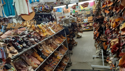 A vibrant shoe store aisle filled with various styles of sandals and shoes on display, with colorful decorations overhead.