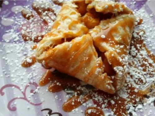 A flaky pastry drizzled with caramel sauce and dusted with powdered sugar on a decorative plate.