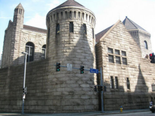 A large stone building with turrets, featuring a mix of architectural styles, set against a clear sky.