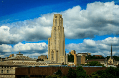 A tall, iconic building stands against a blue sky with fluffy clouds, surrounded by cityscape and greenery.