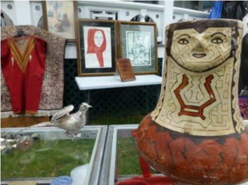 A decorative pottery piece with a face design, surrounded by framed art and traditional clothing on display.