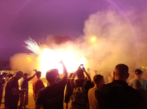 Crowd watching a fireworks display, with smoke and bright sparks lighting up the night sky.