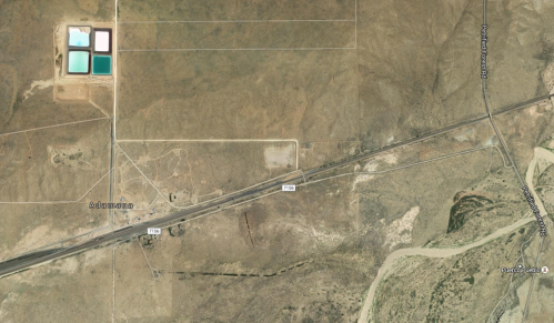 Aerial view of a barren landscape with a highway, sparse vegetation, and several small blue water reservoirs.