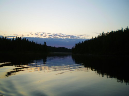 A serene lake at dusk, reflecting trees and a colorful sky with soft clouds.