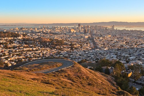 A panoramic view of San Francisco at sunset, showcasing the skyline and winding roads on a hillside.