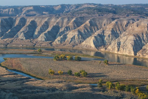 A scenic view of a winding river surrounded by rugged hills and autumn-colored trees in a vast landscape.