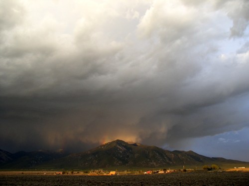 Dramatic clouds loom over a mountain range, with a hint of sunlight breaking through, casting a warm glow on the landscape.