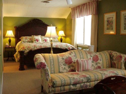 Cozy bedroom with a floral bedspread, two lamps, and a floral-patterned sofa in a green-walled room.
