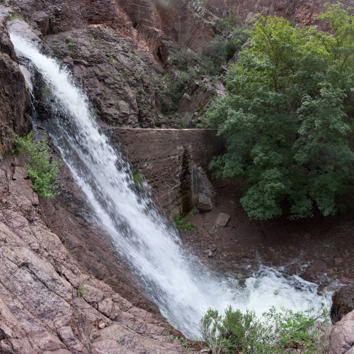 A cascading waterfall flows down rocky terrain, surrounded by lush greenery and steep cliffs.