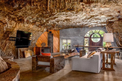 Cozy cave interior featuring a rustic living area with a TV, natural stone walls, and large windows for light.