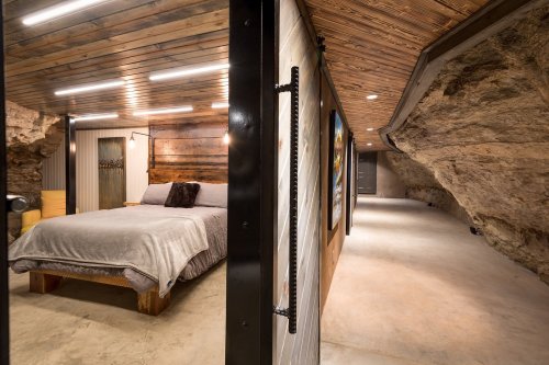 Cozy bedroom with wooden accents and a rock wall, featuring modern lighting and a sleek concrete floor.