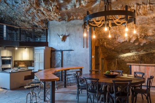 A unique cave kitchen featuring a wooden bar, dining table, and rustic decor with a chandelier and rock walls.