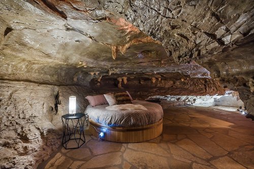 Cozy circular bed in a cave-like room with stone walls and soft lighting, creating a unique, tranquil atmosphere.