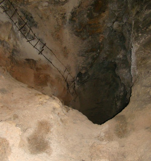 A dark cave with rocky walls and a steep drop, featuring a rusted metal railing along the edge.