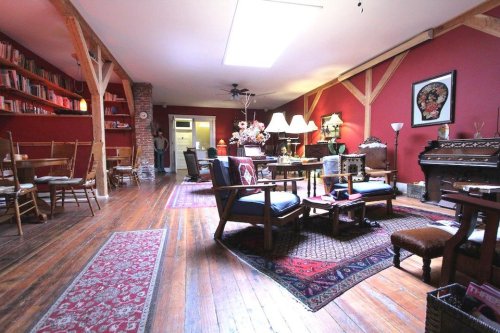 Cozy living space with wooden floors, red walls, bookshelves, and vintage furniture, featuring a warm, inviting atmosphere.