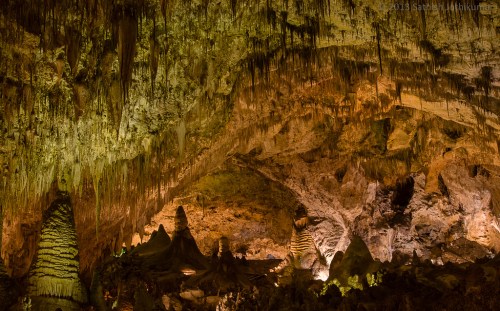 A stunning cave interior featuring stalactites and stalagmites illuminated by warm lighting.