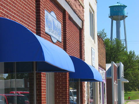 A row of buildings with blue awnings, featuring a water tower in the background against a clear blue sky.