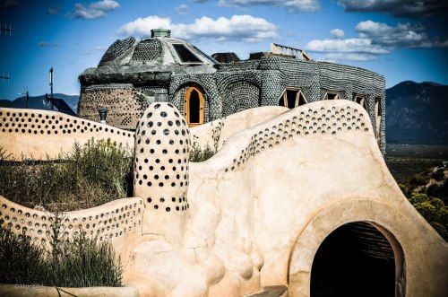 A unique, sculptural building with textured surfaces and rounded shapes, set against a blue sky with clouds.