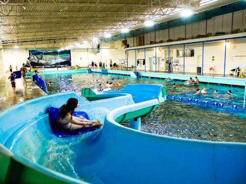 A water slide at an indoor pool with children swimming and playing in the water.