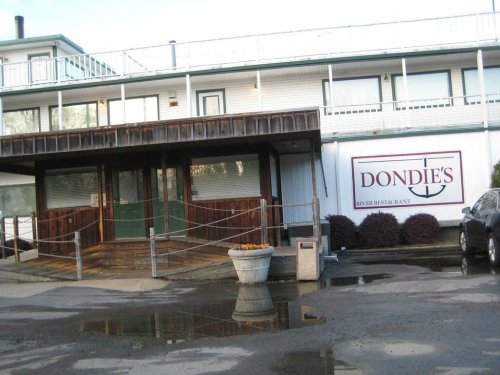 Exterior view of Dondie's River Restaurant, featuring a wooden entrance and a sign, with a reflection in a puddle.