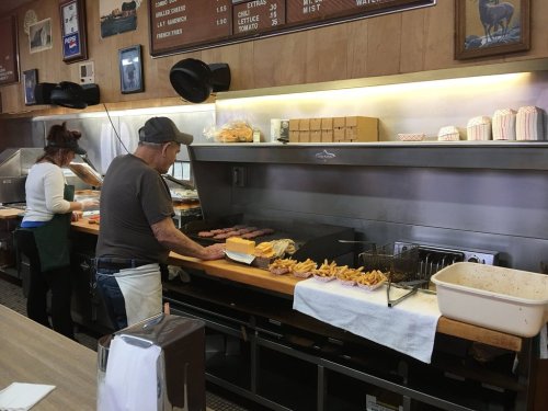 A diner kitchen scene with a cook preparing burgers and fries, while another staff member works in the background.