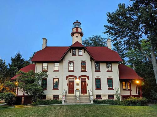 A historic lighthouse keeper's house with a red roof, surrounded by trees, illuminated at dusk.