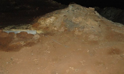 A rocky, uneven terrain with a small mound and some exposed soil, captured in low light.