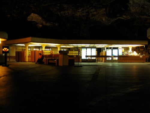 A dimly lit underground space featuring a modern counter and shelves, with a person seated in the background.