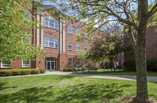 A brick building surrounded by green trees and grass, with a clear blue sky in the background.
