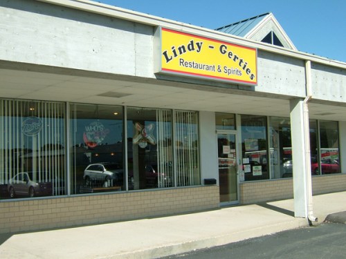 Exterior of Lindy-Gerrie's Restaurant & Spirits, featuring large windows and a colorful sign. Clear blue sky above.