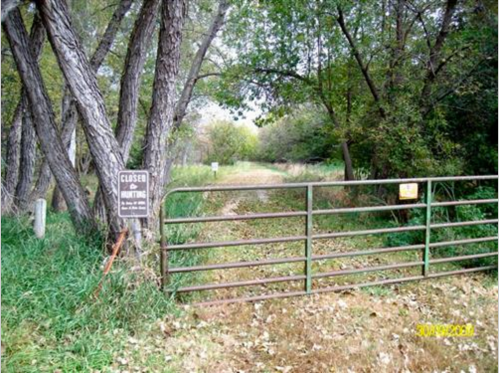 A closed metal gate surrounded by trees and grass, with a sign indicating no hunting allowed.