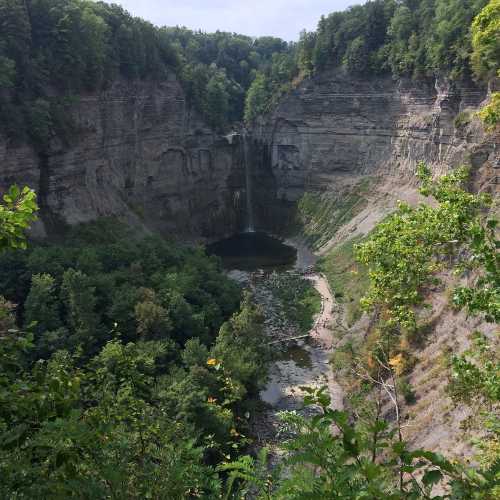 A scenic view of a canyon with a waterfall, surrounded by lush greenery and rocky cliffs.