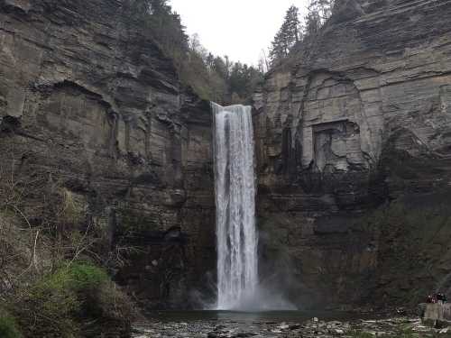 A tall waterfall cascading down rocky cliffs into a serene pool, surrounded by lush greenery and trees.