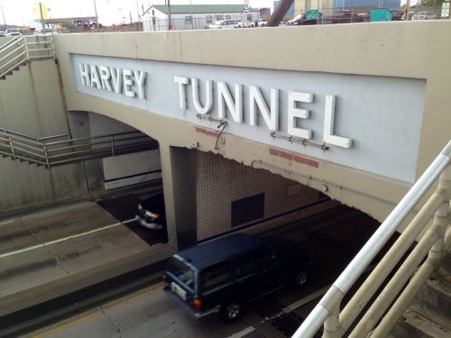 Sign for "Harvey Tunnel" above a roadway with a vehicle passing underneath.