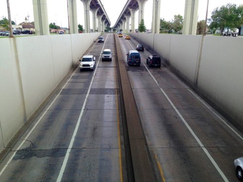 A view of a multi-lane road with vehicles traveling under a raised highway structure.