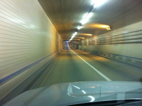 A view from a car driving through a long, illuminated tunnel with smooth, curved walls and a straight road ahead.