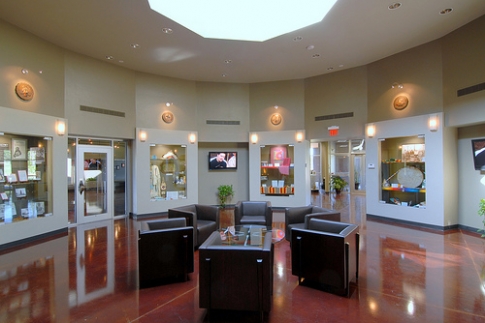 Modern lobby with circular design, seating area, and display cases featuring artwork and information. Bright and inviting atmosphere.