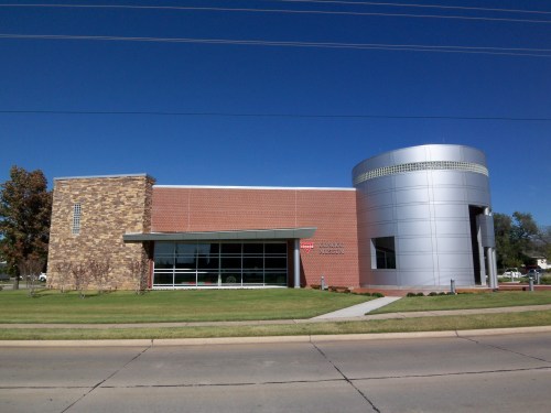 Modern brick and metal building with large windows, set against a clear blue sky and green grass.