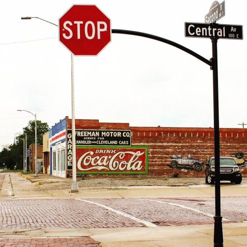 A stop sign at an intersection with vintage buildings and a Coca-Cola advertisement on a brick wall.