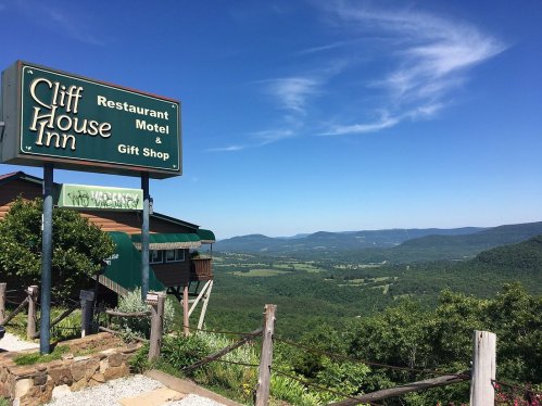 Sign for Cliff House Inn with a scenic view of mountains and valleys under a clear blue sky.