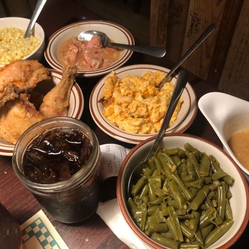 A table spread with fried chicken, green beans, macaroni and cheese, corn, and a drink in a jar.