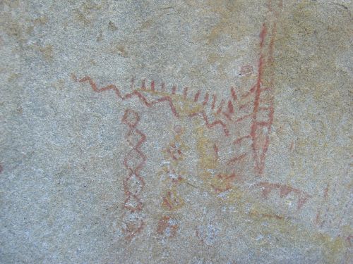 Ancient rock art featuring red and yellow abstract patterns and figures on a stone surface.