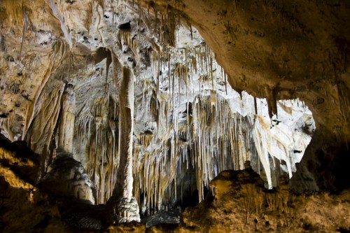 Stalactites and stalagmites in a dimly lit cave, showcasing intricate rock formations and textures.