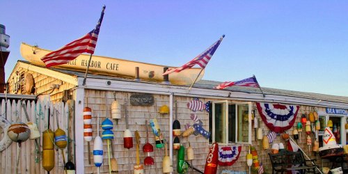 A coastal café adorned with colorful buoys and American flags, set against a clear blue sky.
