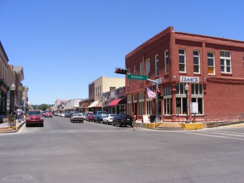A sunny street scene featuring red brick buildings, shops, and cars on a clear day.
